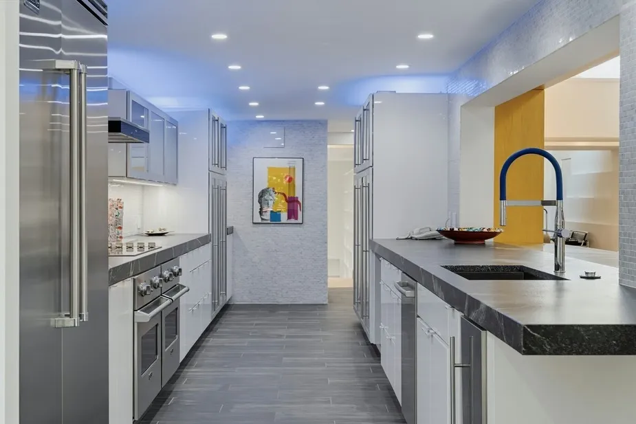 A modern galley kitchen with white cabinetry, stainless steel appliances, dark countertops, and tile flooring.