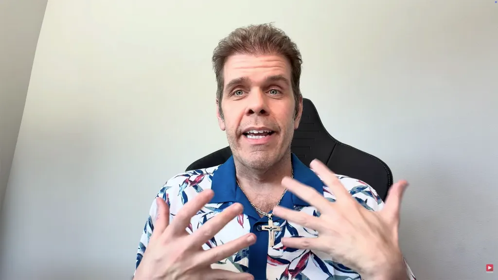 Perez Hilton, a man with light brown hair and a white and blue floral shirt, speaks to the camera.