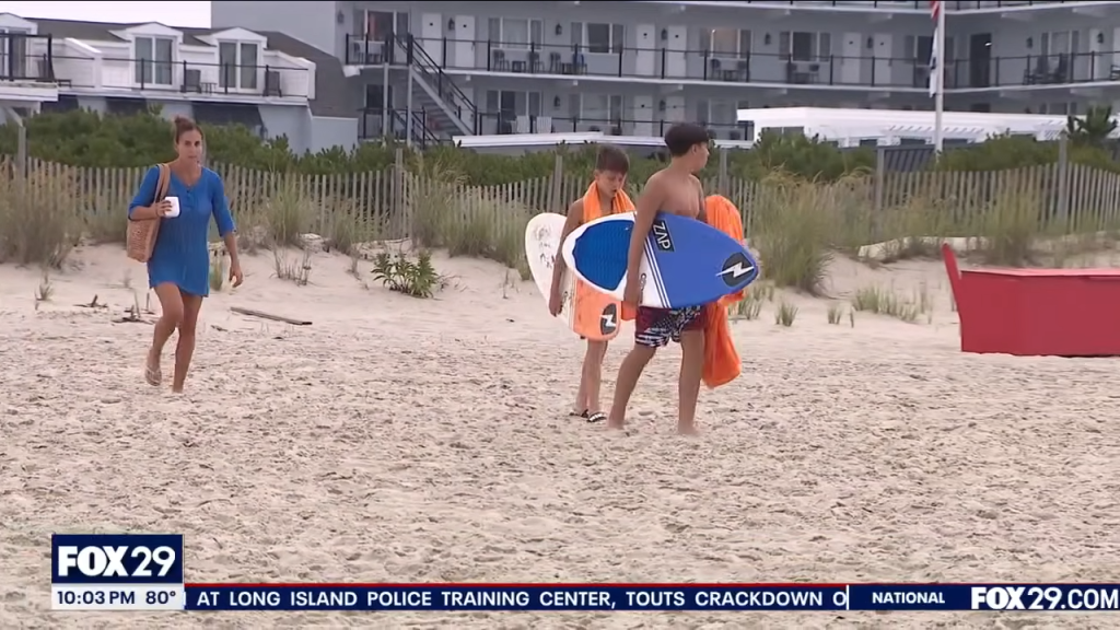 A woman and two teenagers with boogie boards on a sandy beach.