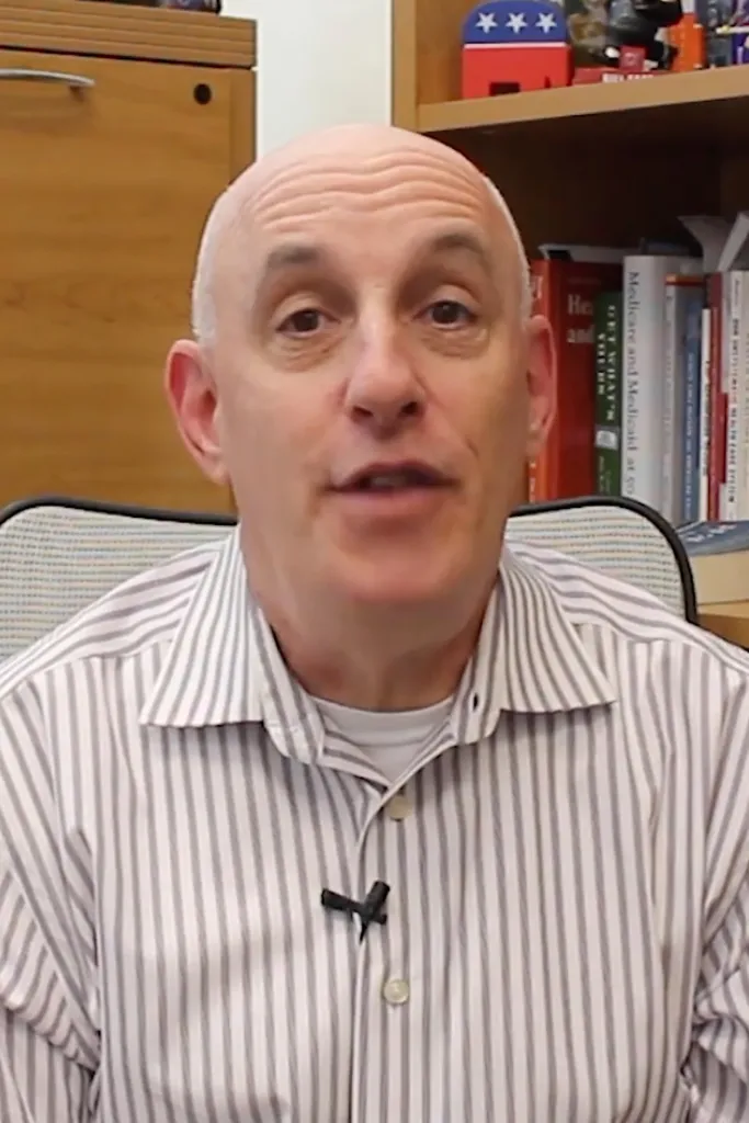 Political Science Professor Richard Himelfarb speaking, with books and a Republican elephant figure visible in the background.