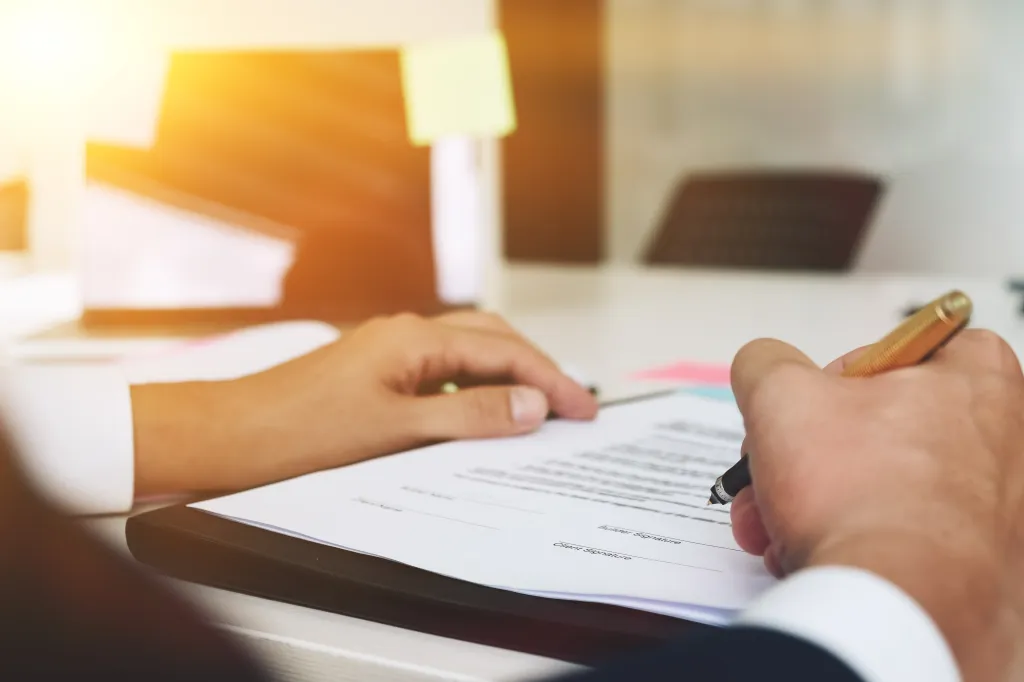 A person's hands signing a document with a pen.