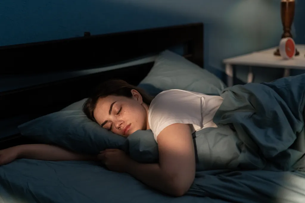 A young woman with freckles sleeping peacefully on a blue pillow at night.