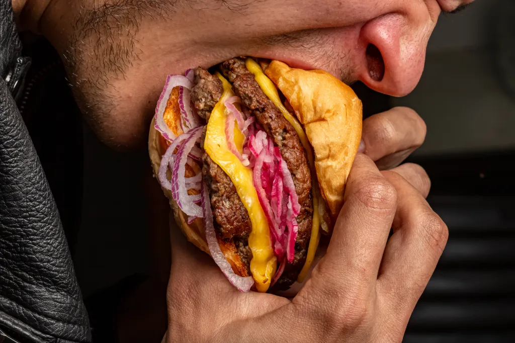 A close-up of a man's face as he takes a large bite out of a hamburger.