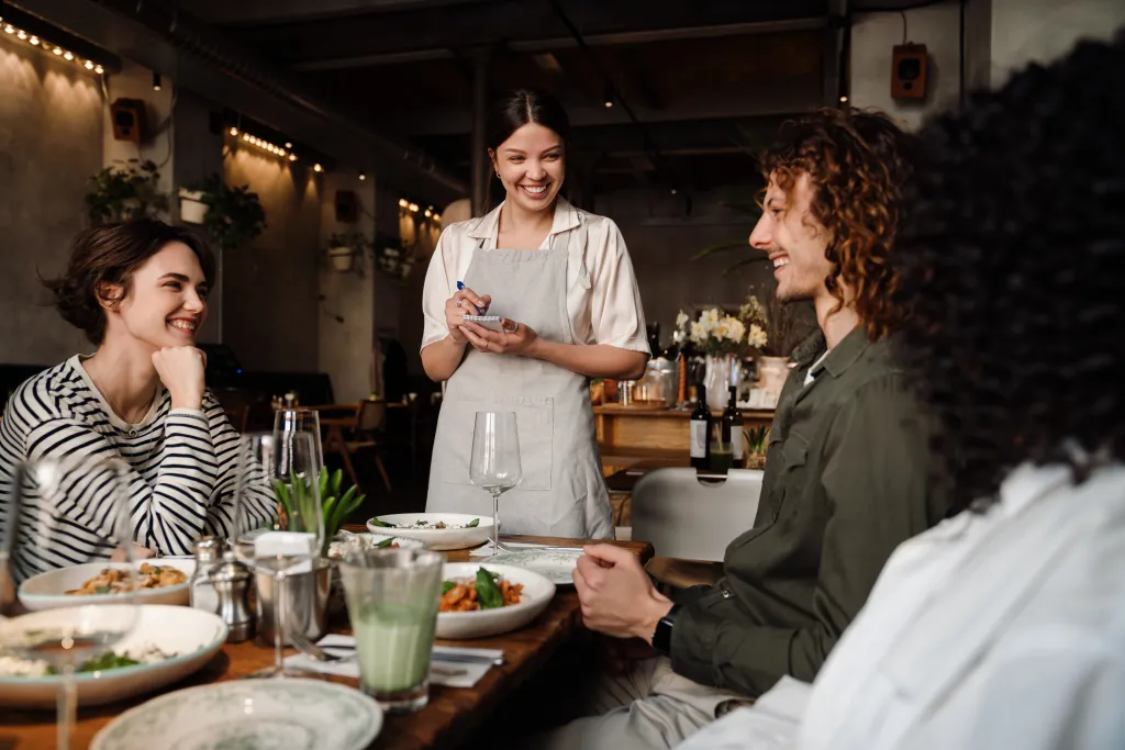 A smiling waitress taking an order from young friends in a restaurant.