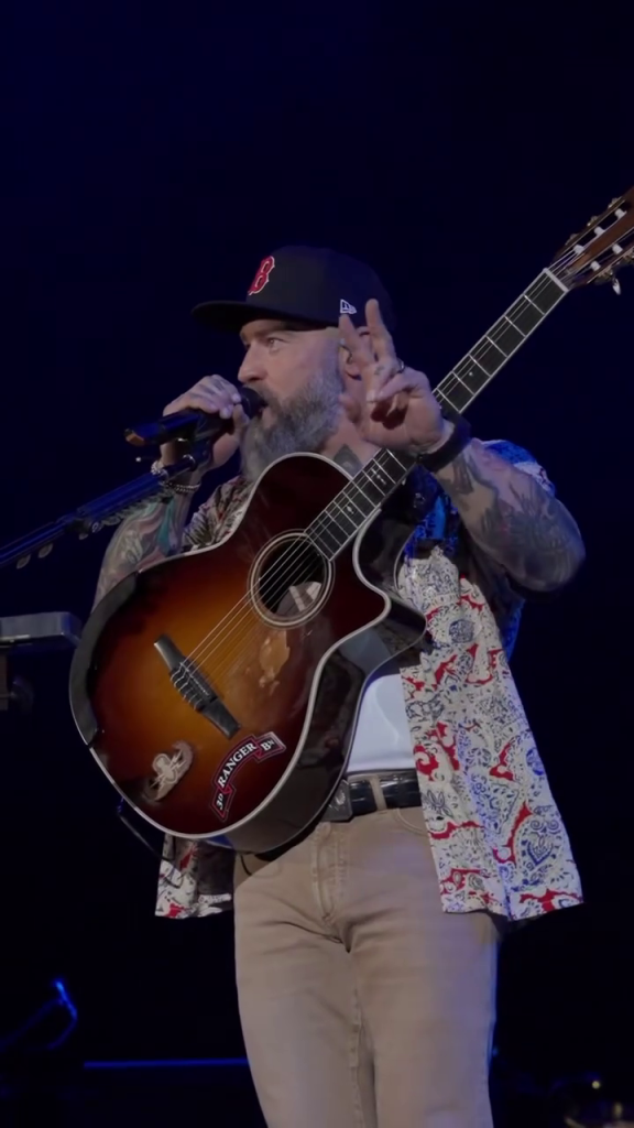 Zac Brown of the Zac Brown Band performs at Fenway Park with a guitar and microphone.