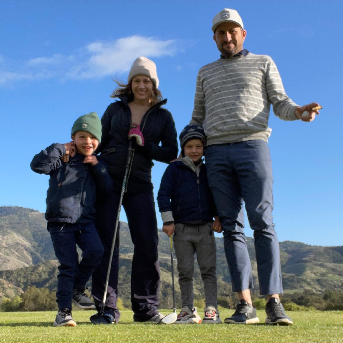 A family of four, including Zach Goldsmith, stands on a golf course with mountains in the background.