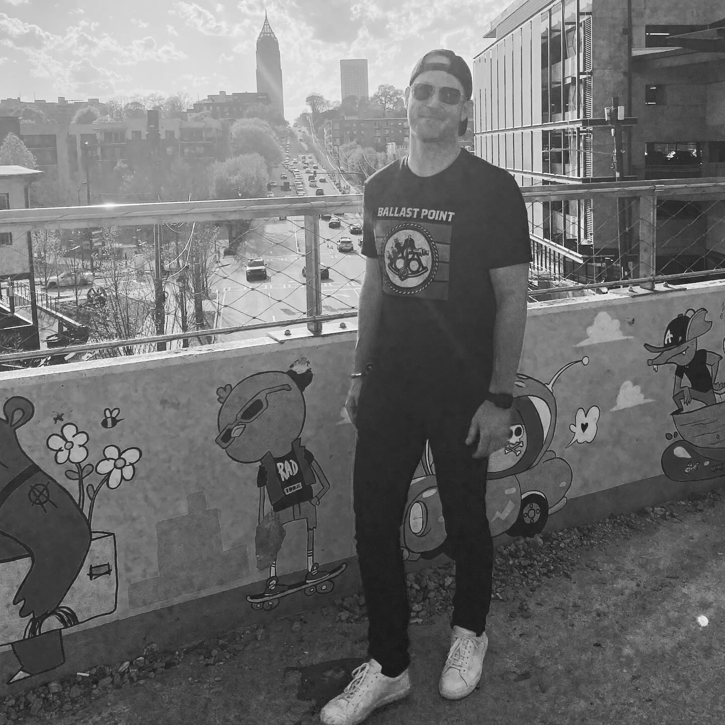 Zach Hickerson in all black stands on a bridge overlooking a city street and skyline.
