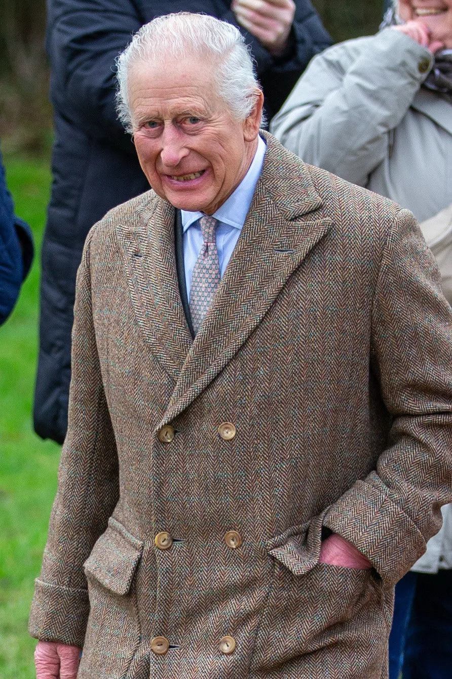 King Charles III smiling and wearing a brown tweed coat.