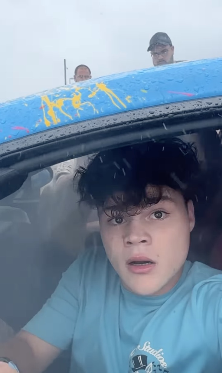 Streamer Jack Doherty appears shocked inside a crashed McLaren supercar as two men peer over the roof.