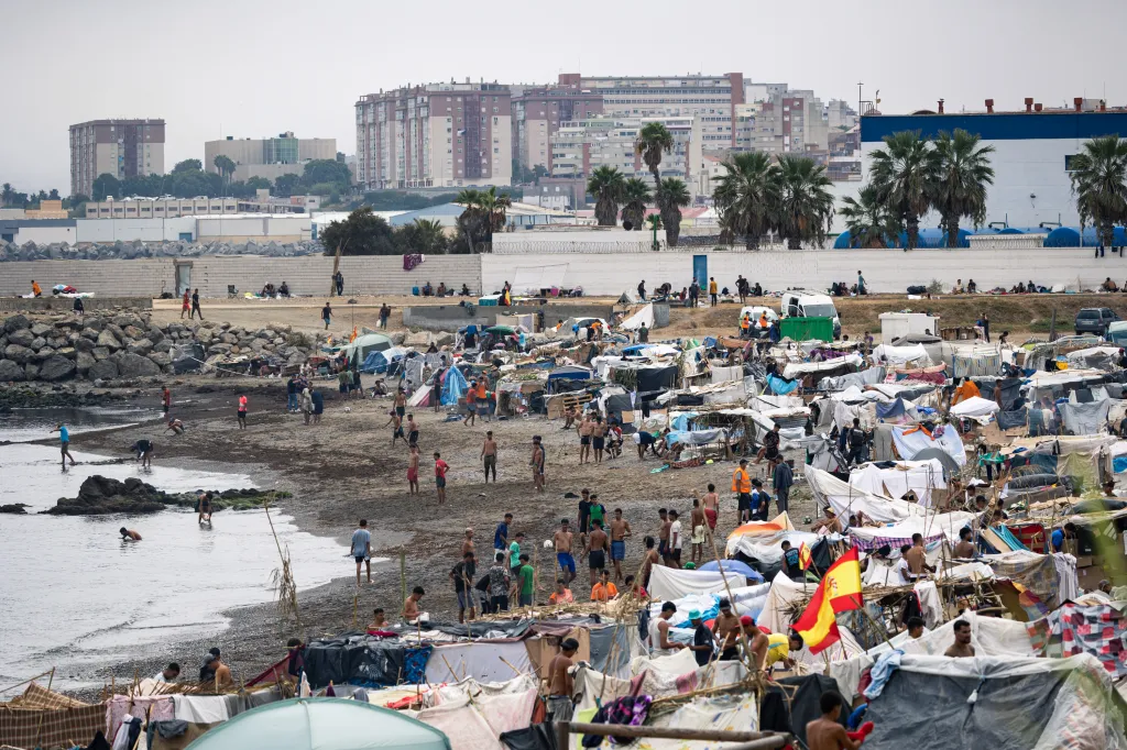 A general view shows a migrant camp of makeshift tents and people on a beach in Ceuta, Spain, with buildings in the background.