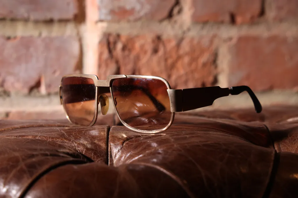 An original pair of Neostyle Nautic 2 sunglasses worn by Elvis Presley resting on a leather surface against a brick wall.