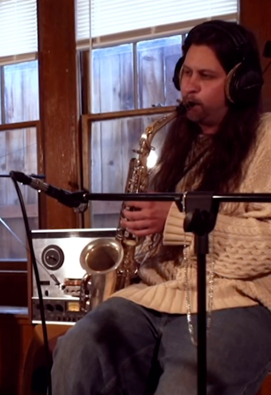 Nathaniel Young performing on a saxophone while wearing headphones.