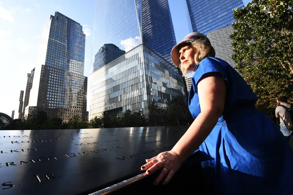 Mary Kay Linge touches a memorial at the World Trade Center with skyscrapers in the background.