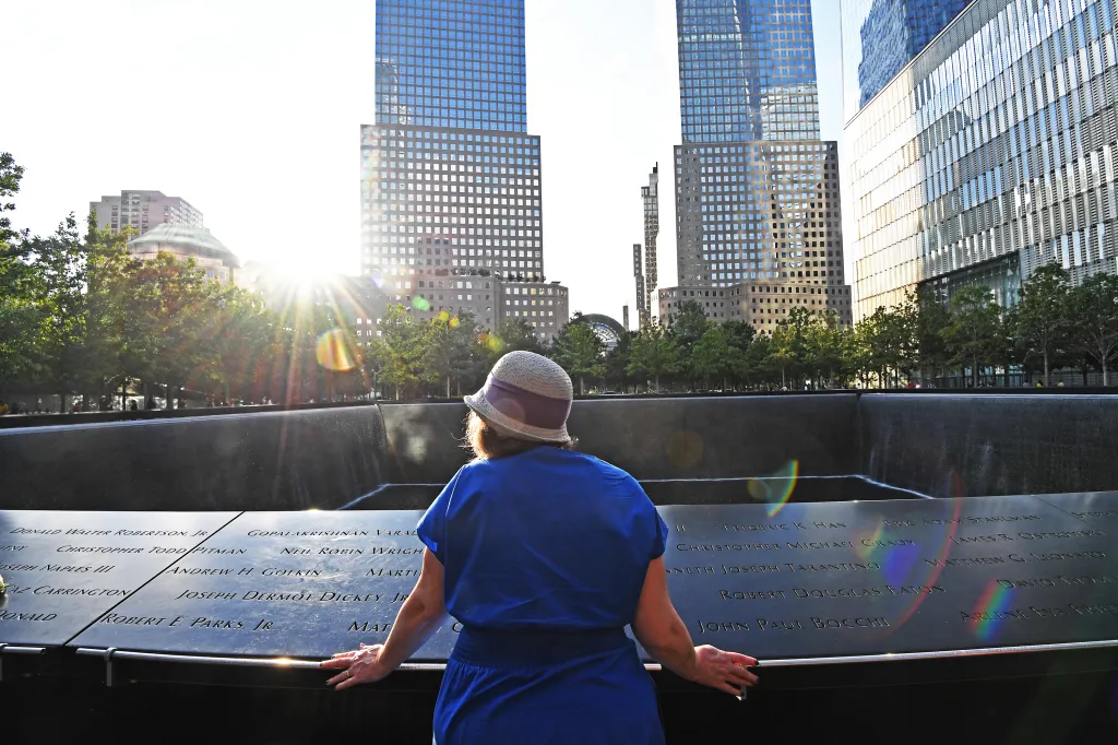 Mary Kay Linge, a New York Post writer, wearing a blue dress and a hat, stands at the World Trade Center memorial.