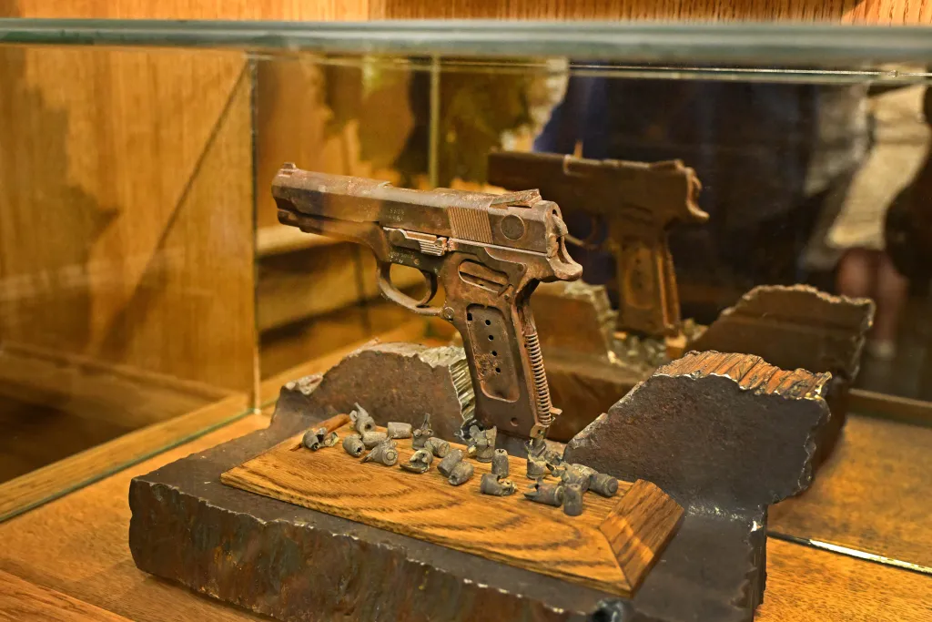 A rusted gun and fragmented bullets displayed in a glass case.