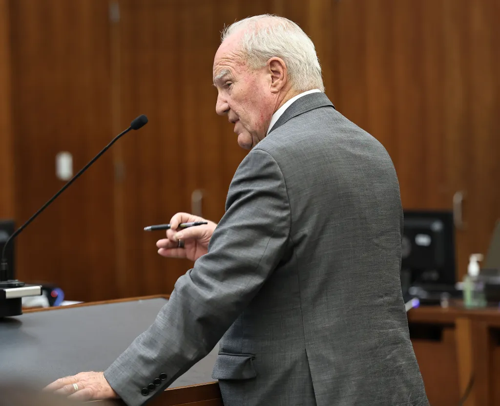 An older man in a gray suit speaks into a microphone from a podium.