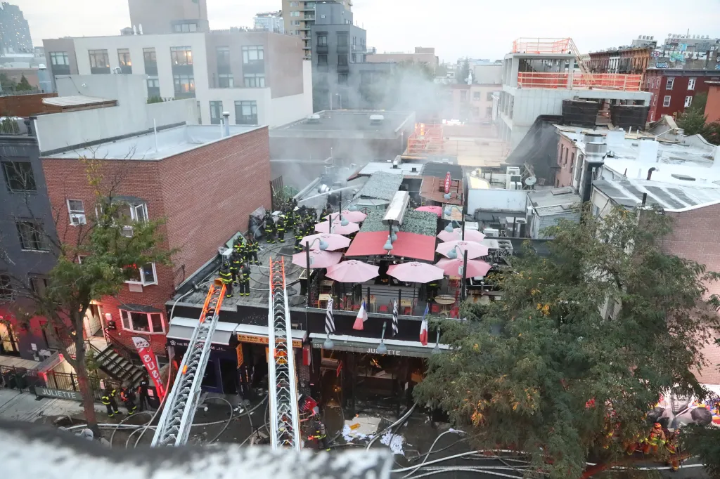 Firefighters responding to a fourth-alarm fire at a restaurant in Brooklyn, with visible smoke and two extended ladders.