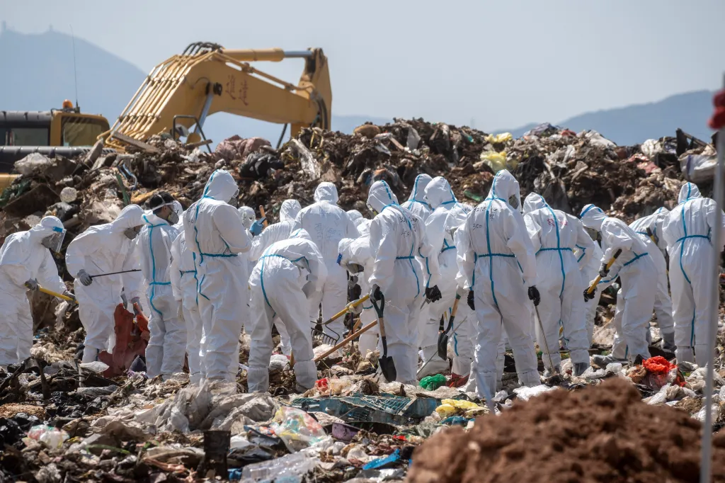 Police officers in personal protective equipment search a landfill.