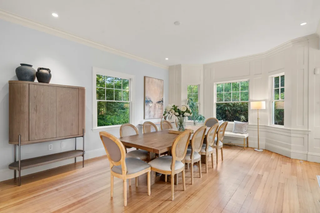 The dining room of Julia Child's former home with a long wooden table and chairs, large windows, and light hardwood floors.