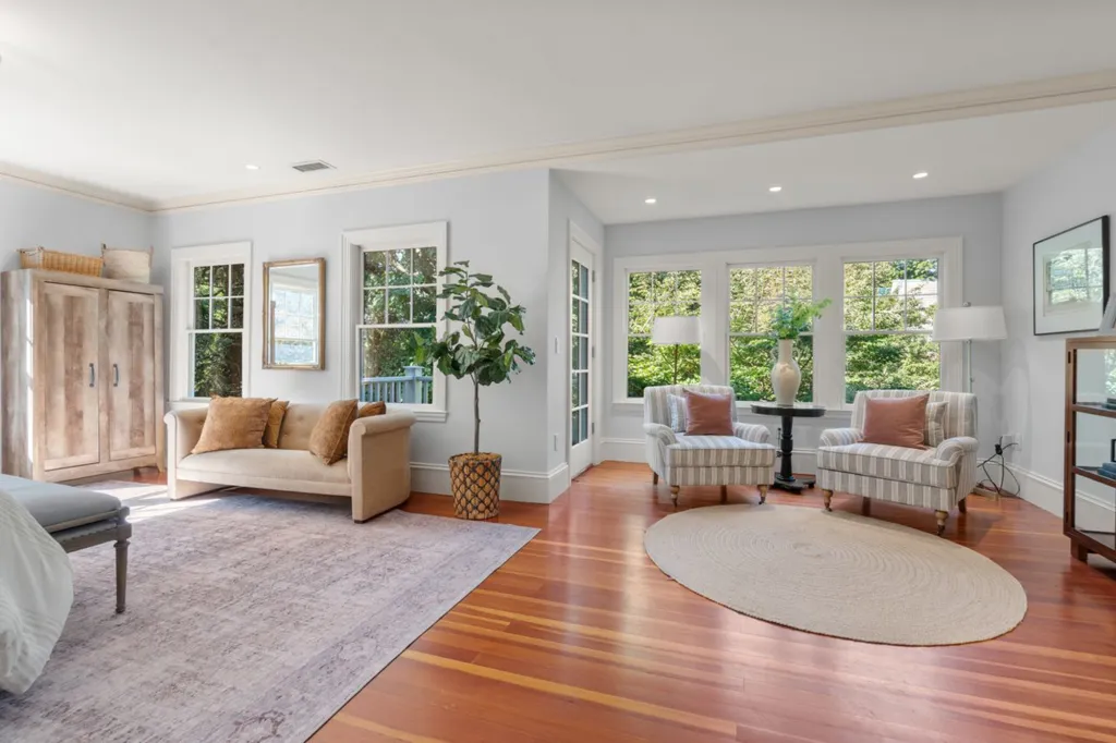 The sitting room in Julia Child's former home has wood floors, light blue walls, two sitting areas, and multiple windows.