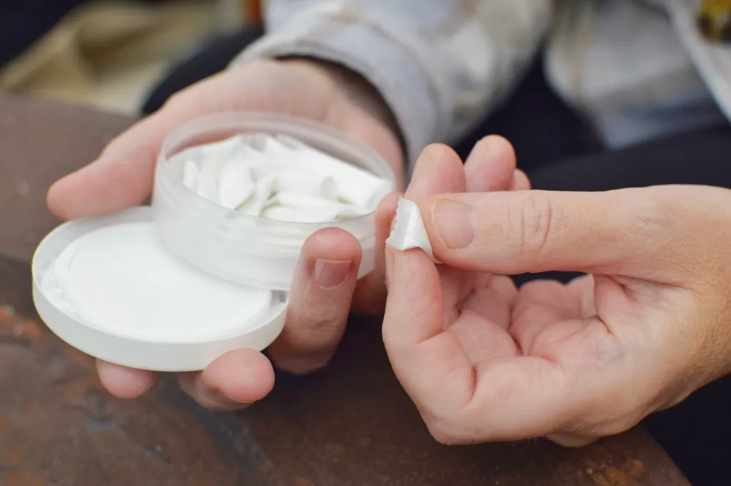 A person holding an open container of white nicotine pouches and taking one out.