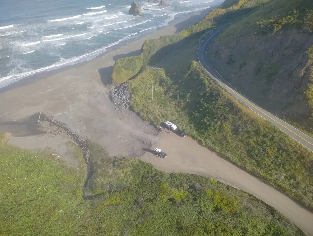 Aerial view of the California coastline with a highway curving along the cliffs and a sandy beach next to the ocean.