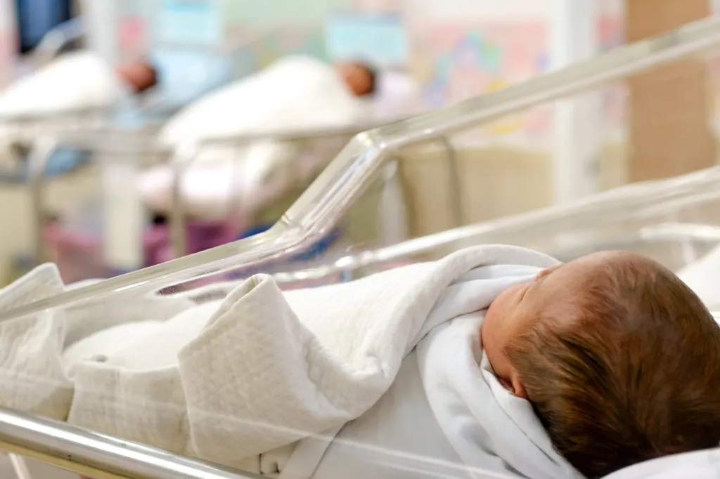 Newborn baby in a hospital bassinet, wrapped in a white blanket.