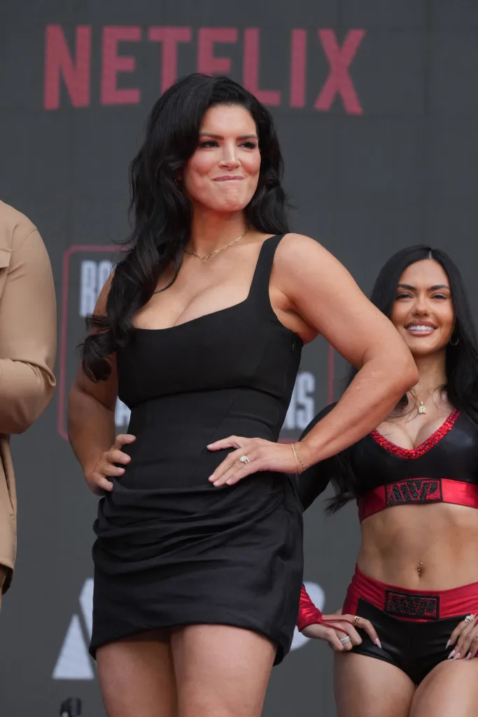 Gina Carano on a stage with a Netflix logo in the background.