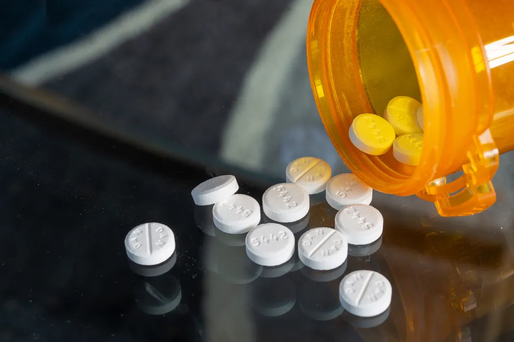 White and yellow pills spilled from an orange pill bottle onto a dark surface.