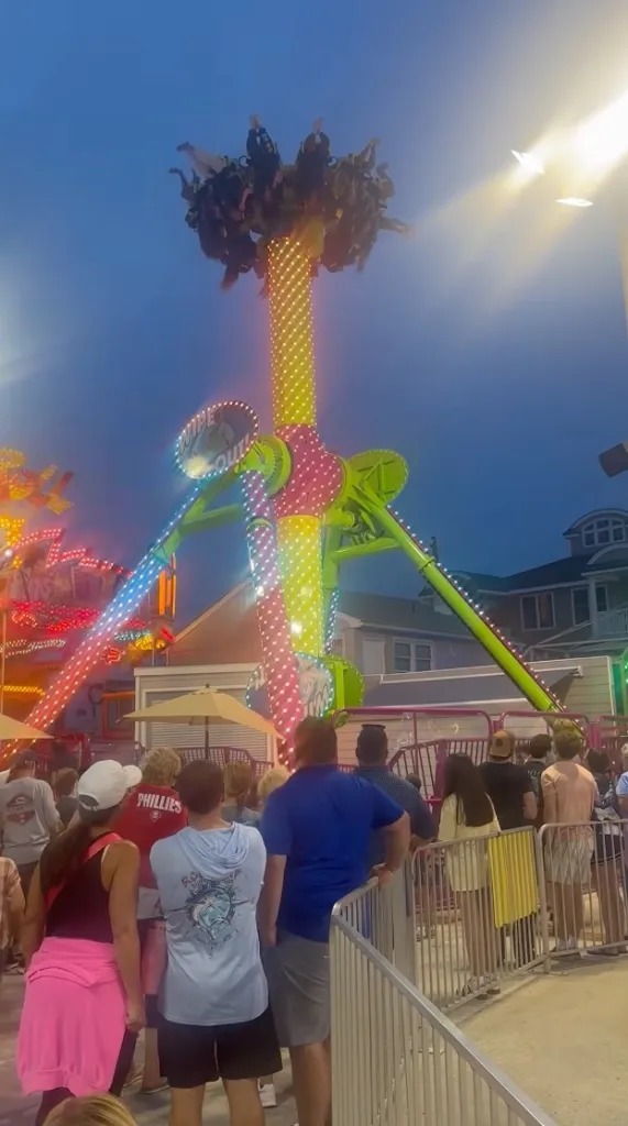 People riding a brightly lit carnival ride at night.
