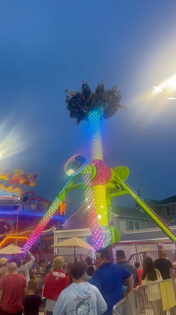 People riding a brightly lit carnival ride against a blue night sky.