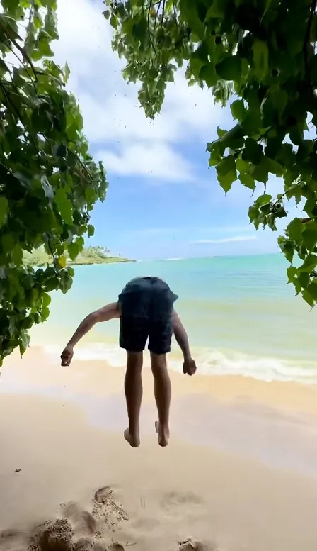 Person doing a handstand on a sandy beach, with their head hidden behind a bush.