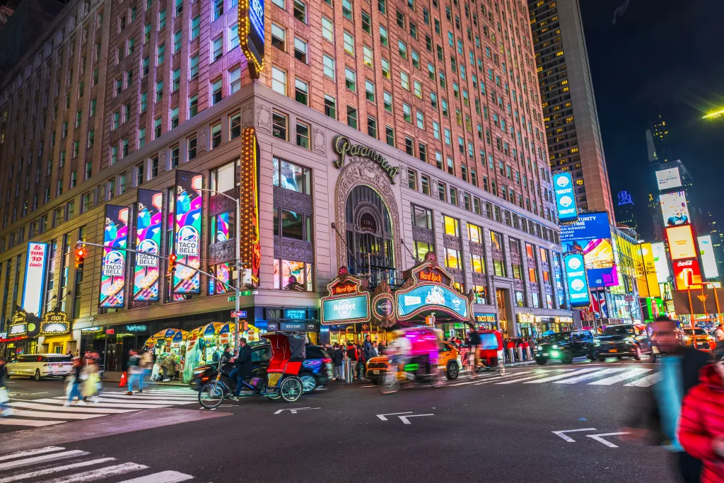 Busy intersection at night in Times Square with illuminated Hard Rock Cafe, Taco Bell, and Paramount building.