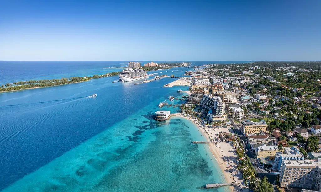 Panoramic drone view of Nassau City and Paradise Island, Bahamas, showing turquoise waters, cruise ships, and coastal resorts.