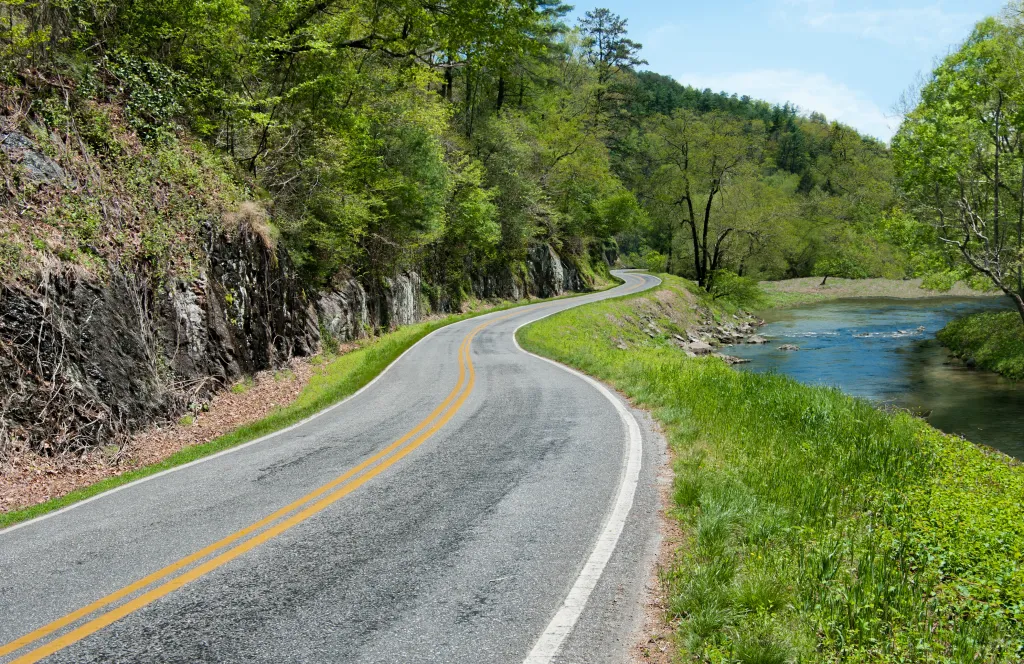 Winding North Carolina byway next to a flowing stream and rocky outcropping.
