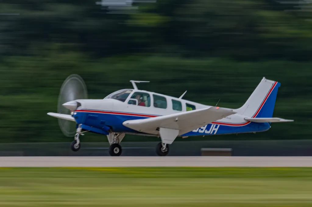 Blue and white Beechcraft Bonanza aircraft taking off with motion blur.