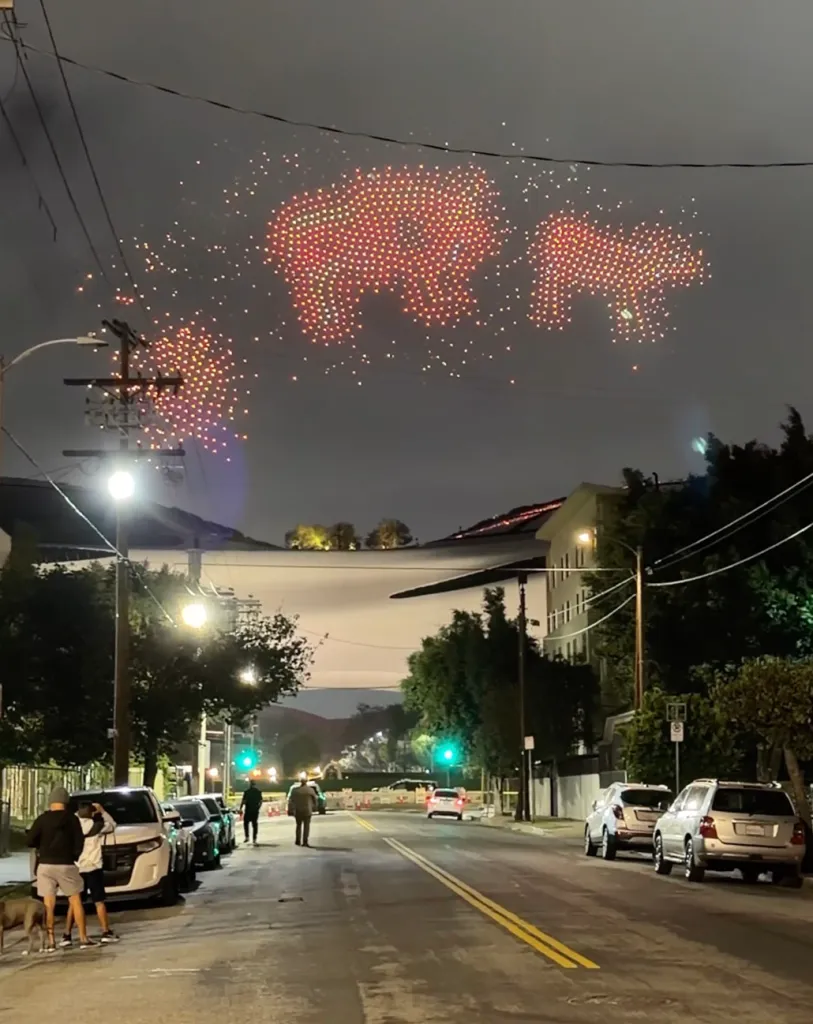 Drone light show forming the shapes of three bears in the night sky over a residential street.