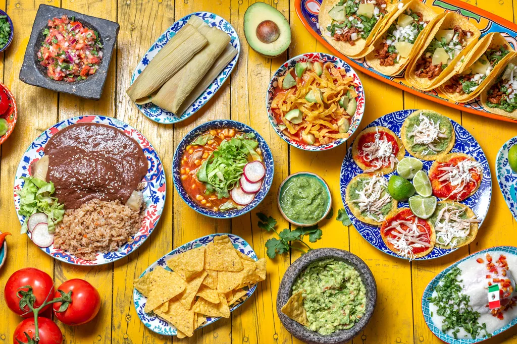 Mexican food spread with tacos, tamales, enchiladas, and guacamole.