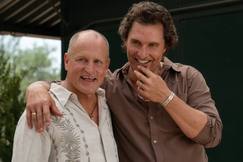 Matthew McConaughey and Woody Harrelson smiling, with Harrelson wearing a beige shirt and McConaughey wearing a brown shirt.