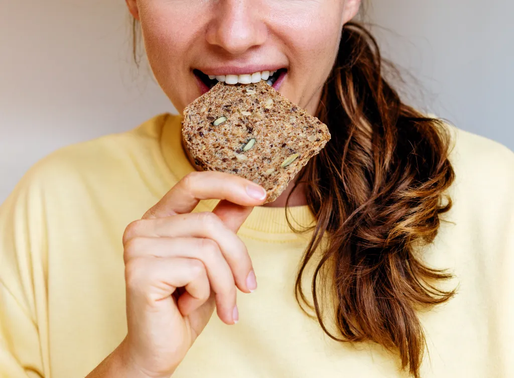 Woman taking a bite out of a piece of grain bread.