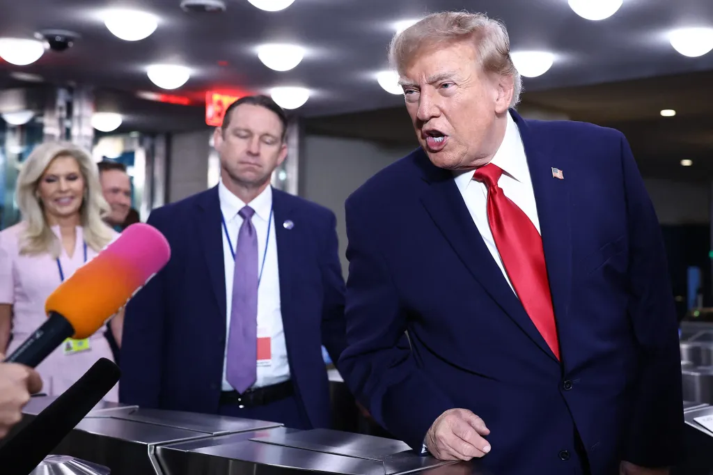 Donald Trump speaking into a microphone with three other people in the background.