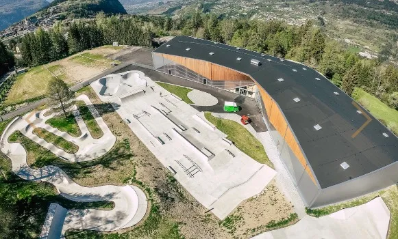 Aerial view of a pump track and skatepark next to a large building with a curved roof.