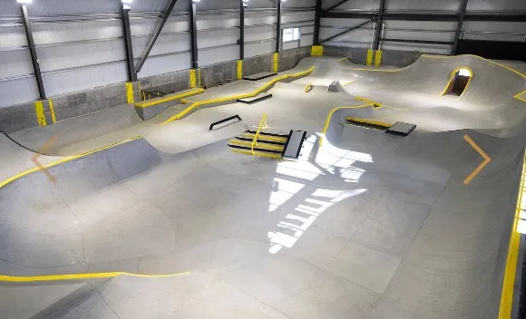 An indoor skatepark with various concrete ramps and rails, highlighted with yellow trim.