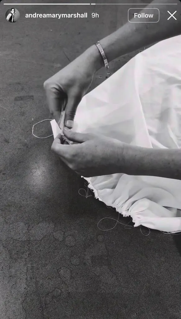 A person's hands sewing a white garment with a needle and thread.