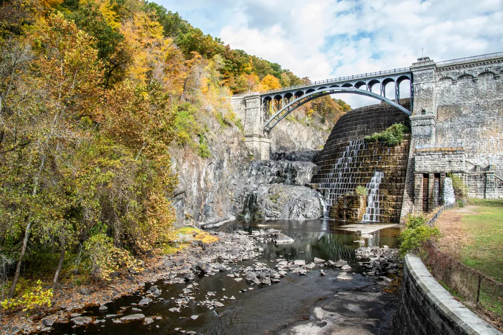 Croton Gorge Park with a stone arch bridge and waterfall during autumn.