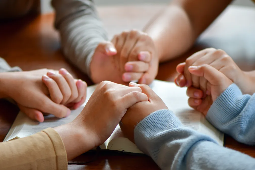 Hands clasped in prayer over an open Bible.