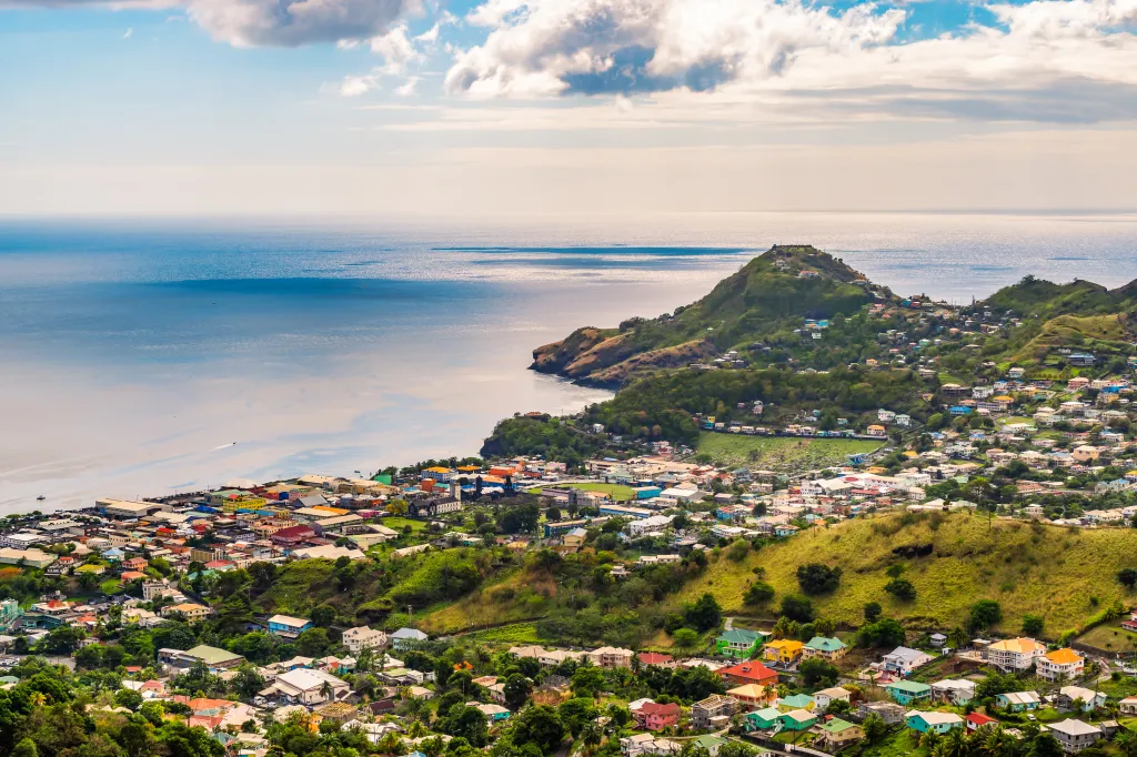 Aerial view of Kingstown, Saint Vincent and the Grenadines, showing colorful buildings on green hillsides sloping down to a bay with blue water.