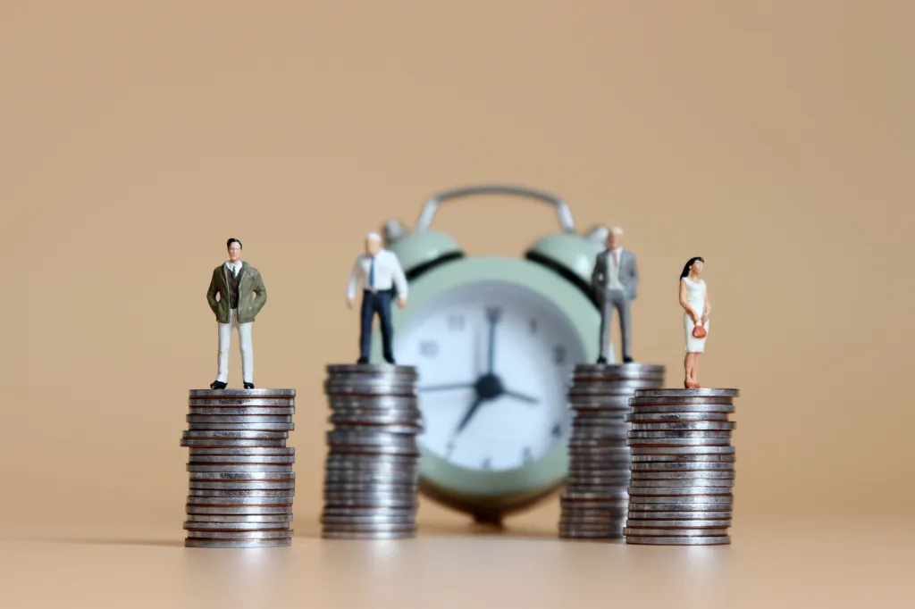 Miniature figures of people standing on stacks of coins in front of an alarm clock.