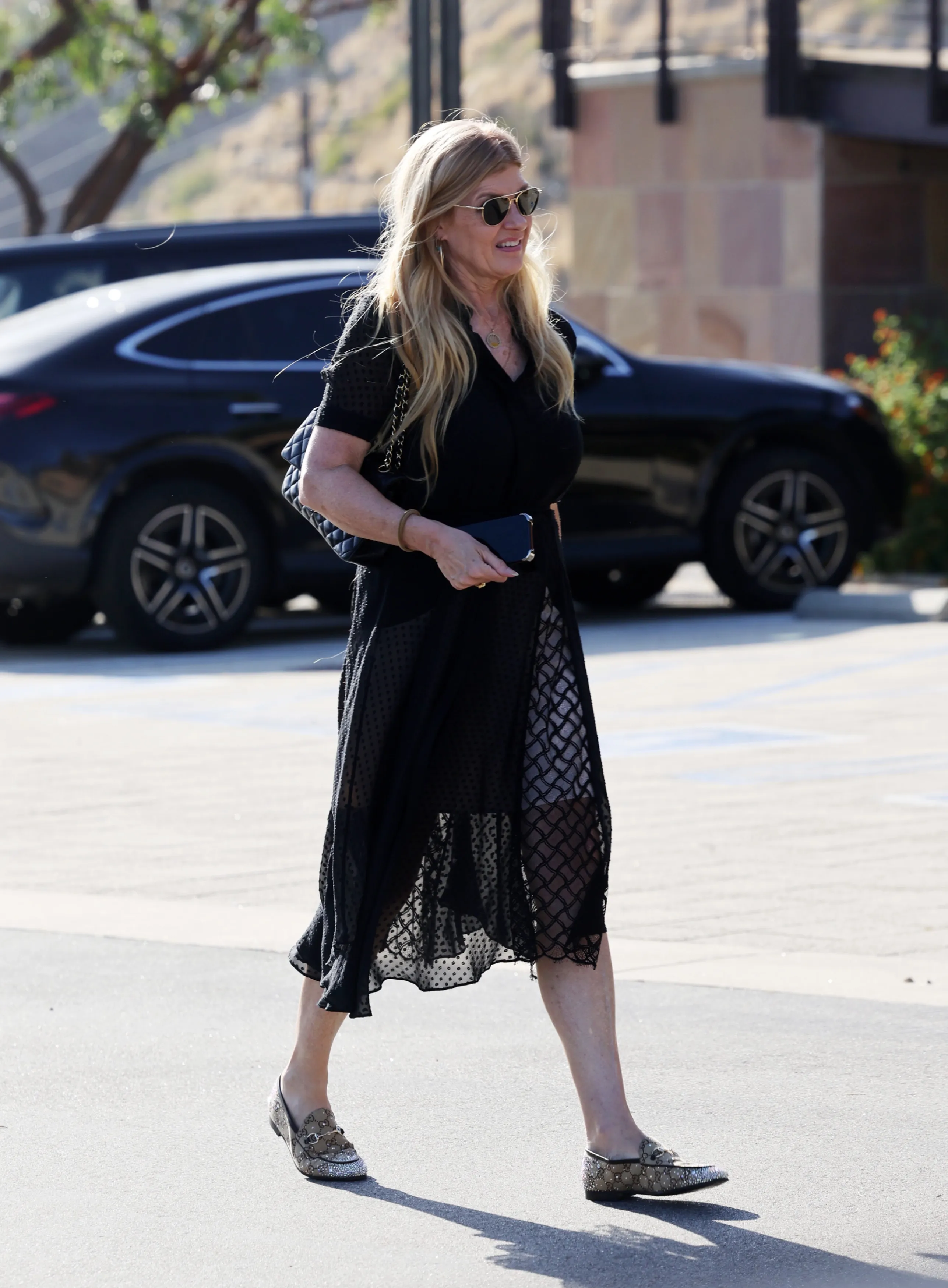 Connie Britton in a black sheer dress, sunglasses, and Gucci loafers at a celebration of life.