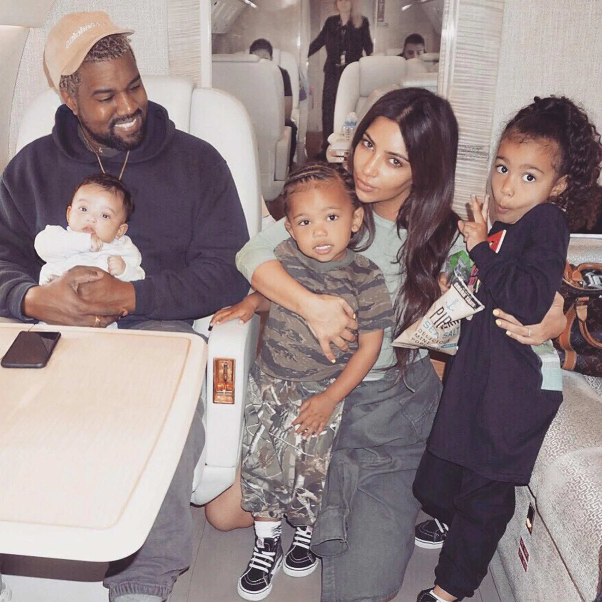 Kanye West holds his baby while Kim Kardashian poses with their two other children on a private jet.